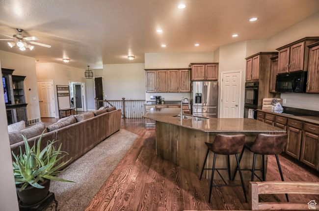 Kitchen with black appliances, a sink, a center island with sink, dark wood-style flooring, and open floor plan | Image 6