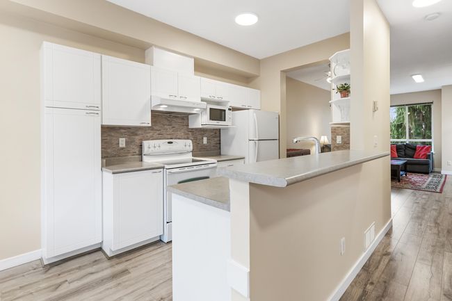 Kitchen featuring light wood-style floors, under cabinet range hood, white appliances, and white cabinets | Image 14