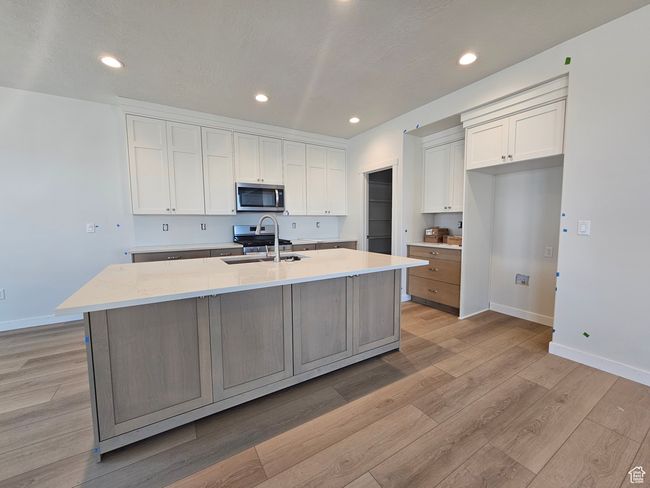 Kitchen featuring stainless steel appliances, white cabinets, a center island with sink, light wood-style flooring, and recessed lighting | Image 7