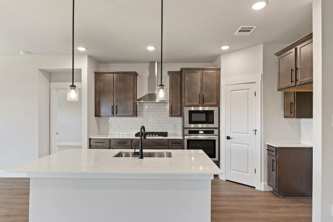 Kitchen featuring stainless steel appliances, wall chimney exhaust hood, backsplash, dark brown cabinetry, and recessed lighting | Image 5