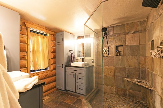 master bathroom featuring glass shower area, vanity, a tile shower, stone finish floors, and rustic walls | Image 22