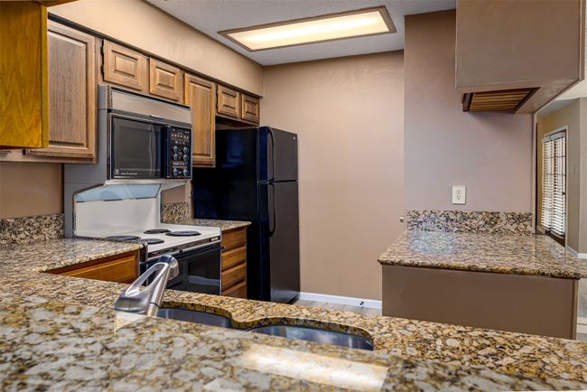 Kitchen with light stone counters, a sink, black appliances, brown cabinets, and baseboards | Image 5