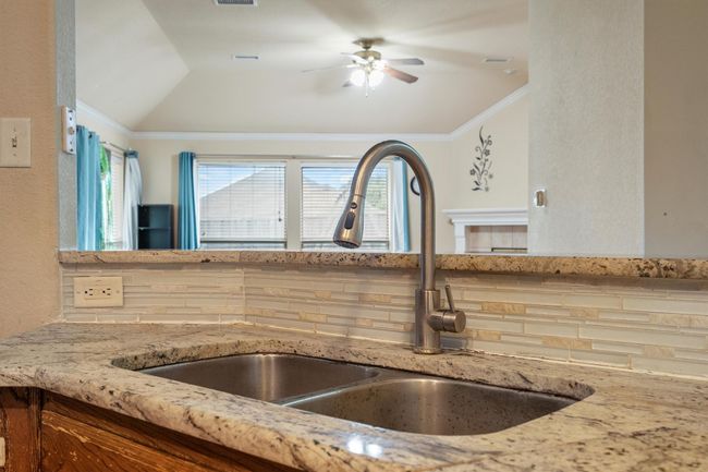 Kitchen view of light stone countertops, a ceiling fan, crown molding, and a textured wall | Image 18