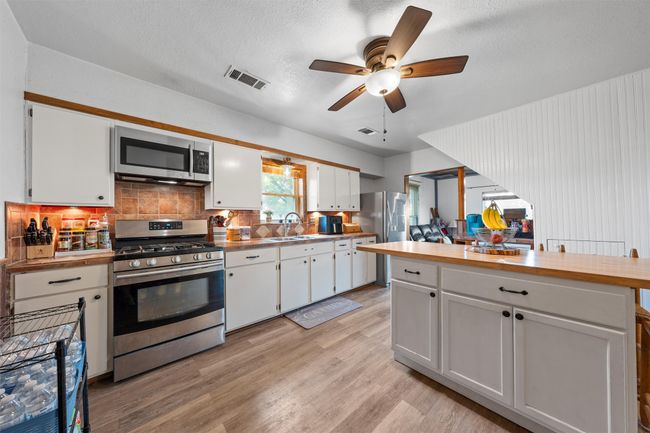Kitchen featuring white cabinetry, stainless steel appliances, a sink, light wood finished floors, and visible vents | Image 5