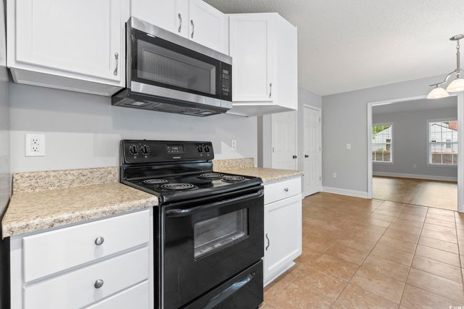 Kitchen featuring black electric range, stainless steel microwave, light countertops, white cabinetry, and a textured ceiling | Image 13