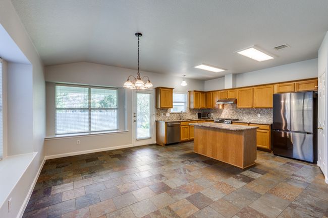Kitchen featuring stainless steel appliances, under cabinet range hood, stone tile floors, tasteful backsplash, and a center island | Image 11