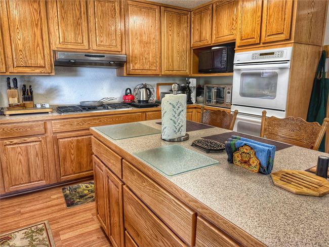 Kitchen featuring brown cabinetry, black microwave, stainless steel gas stovetop, and under cabinet range hood | Image 13