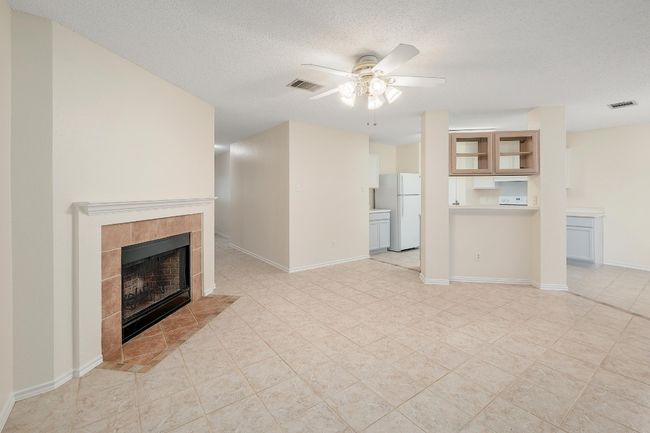 Unfurnished living room with ceiling fan, a fireplace, a textured ceiling, baseboards, and light tile patterned floors | Image 5