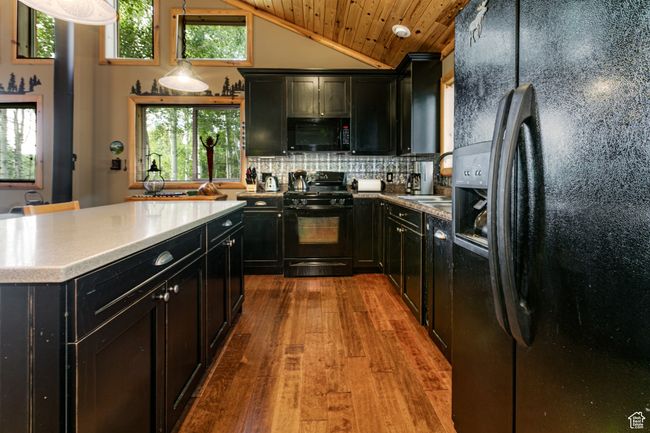Kitchen with black appliances, dark cabinets, hardwood / wood-style floors, vaulted ceiling, and decorative backsplash | Image 14