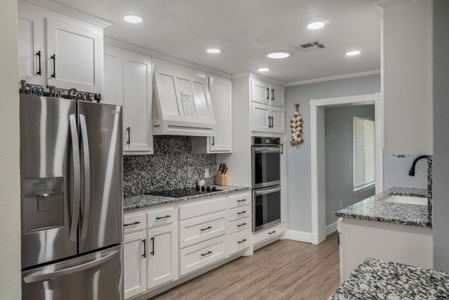 Kitchen with stainless steel appliances, ornamental molding, white cabinets, light stone counters, and decorative backsplash | Image 6