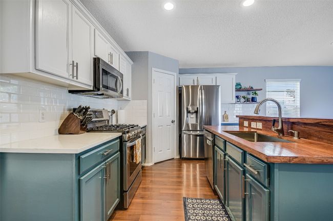 Kitchen featuring appliances with stainless steel finishes, white cabinetry, wood finished floors, tasteful backsplash, and a textured ceiling | Image 8
