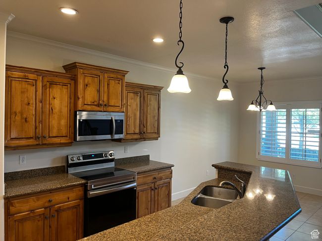 Kitchen with appliances with stainless steel finishes, brown cabinets, light tile patterned floors, crown molding, and hanging light fixtures | Image 20