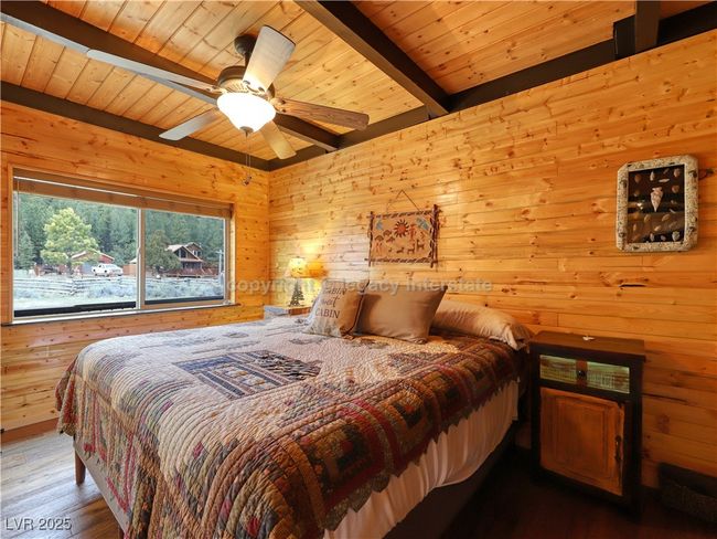 Bedroom with beam ceiling, ceiling fan, wooden walls, wood ceiling, and hardwood / wood-style flooring | Image 16