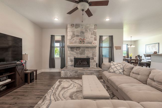 Living room with a ceiling fan, dark wood-style floors, a stone fireplace, and a chandelier | Image 6