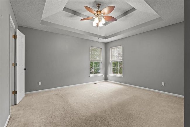 Empty room featuring a tray ceiling, carpet floors, a ceiling fan, and a textured ceiling | Image 17