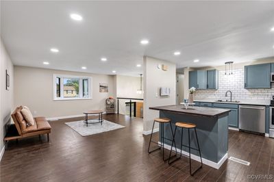 Kitchen featuring dark wood-type flooring, sink, blue cabinetry, appliances with stainless steel finishes, and decorative light fixtures | Image 1