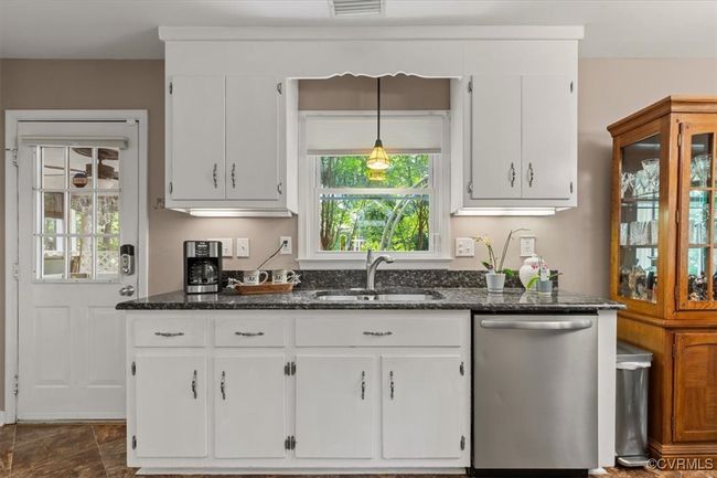 Kitchen featuring stainless steel dishwasher, white cabinetry, a sink, dark stone counters, and hanging light fixtures | Image 16