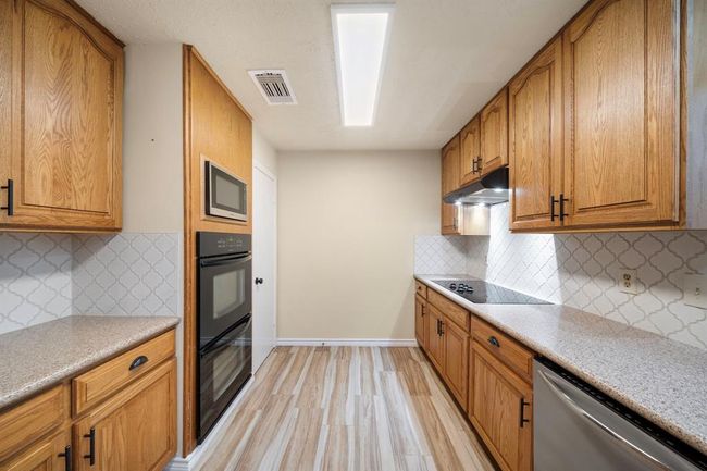 Enjoy ample counter space and extensive storage in this well-appointed kitchen, featuring wood cabinetry, granite countertops, and a modern tile backsplash. | Image 12