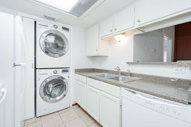 Laundry area featuring a sink, stacked washing maching and dryer, light tile patterned floors, visible vents, and laundry area | Image 7