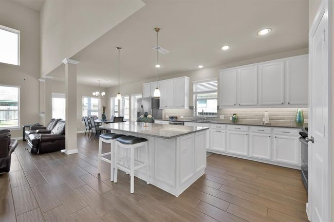 If you head down the hall you'll meet your elegant future kitchen. This entertainer's kitchen is complete with white cabinetry, pendant and recessed lighting, a stylish and modern backsplash, and a large island to set this kitchen apart from the competition. | Image 7