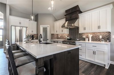 Kitchen featuring backsplash, ventilation hood, sink, vaulted ceiling, and a center island with sink | Image 2