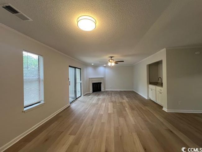 Unfurnished living room with a textured ceiling, ornamental molding, wood finished floors, and visible vents | Image 29