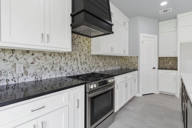 Kitchen featuring stainless steel gas range, custom exhaust hood, white cabinetry, backsplash, and dark stone countertops | Image 15