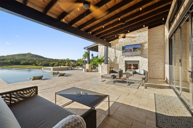 View of patio featuring a water view, a ceiling fan, and an outdoor living space with a fireplace | Image 9