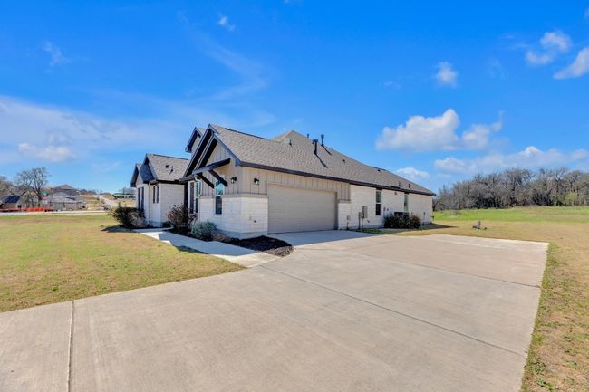 View of side of property with an attached garage, a shingled roof, concrete driveway, a lawn, and board and batten siding | Image 4