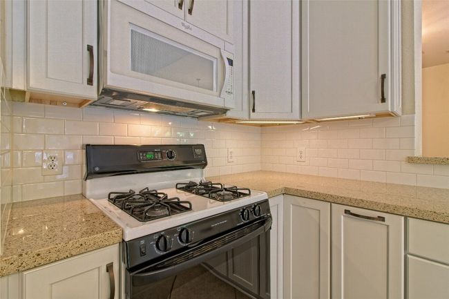 Kitchen featuring gas range oven, white microwave, backsplash, light stone counters, and white cabinetry | Image 19