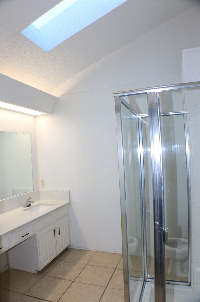 Bathroom featuring a skylight, vanity, lofted ceiling, a stall shower, and tile patterned flooring | Image 25