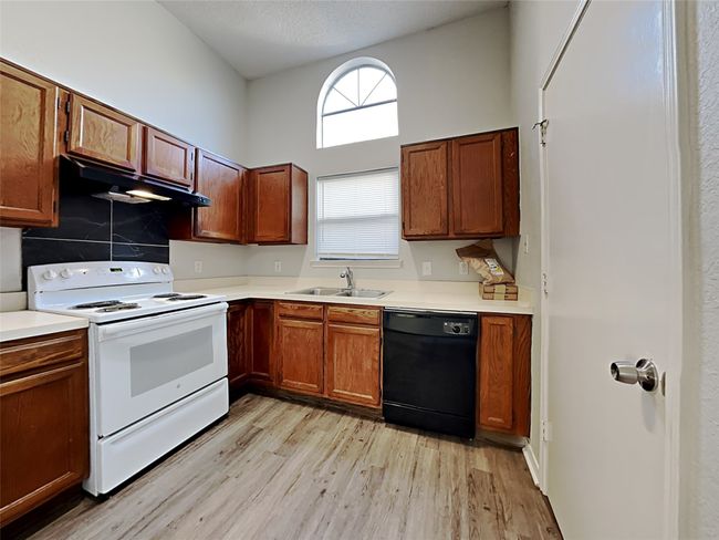 Kitchen featuring white range with electric stovetop, black dishwasher, under cabinet range hood, and light wood-style flooring | Image 4