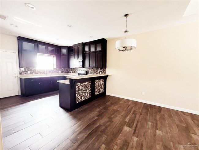 Kitchen with a peninsula, glass insert cabinets, decorative backsplash, dark wood-style flooring, and hanging light fixtures | Image 9