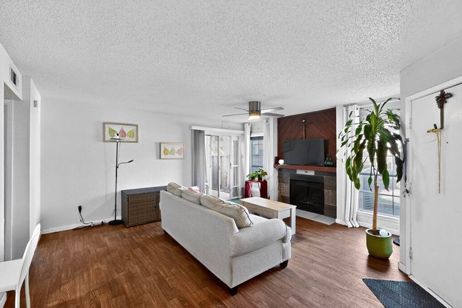 Living room with a textured ceiling, dark wood-type flooring, a fireplace with flush hearth, and a ceiling fan | Image 5