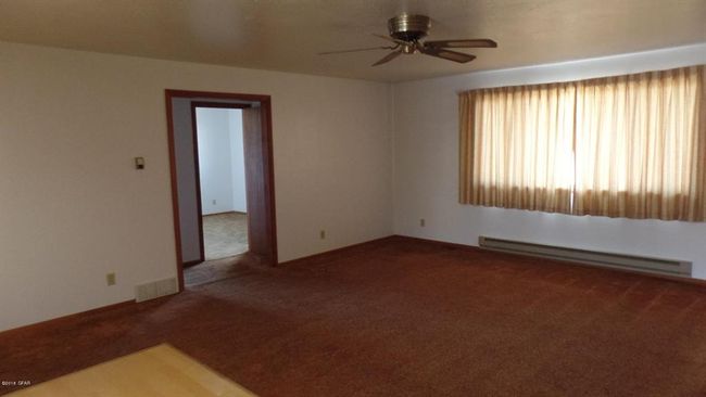 Carpeted living room with visible vents, ceiling fan, and a baseboard heating unit | Image 24
