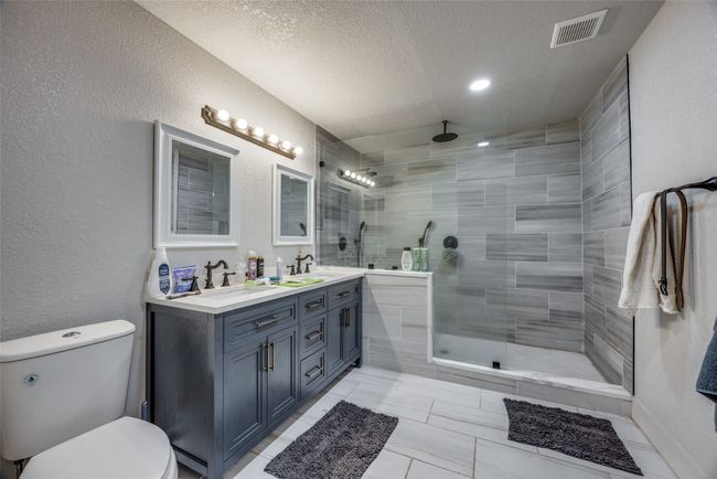 Full bathroom with toilet, a textured ceiling, tiled shower, double vanity, and a textured wall | Image 6