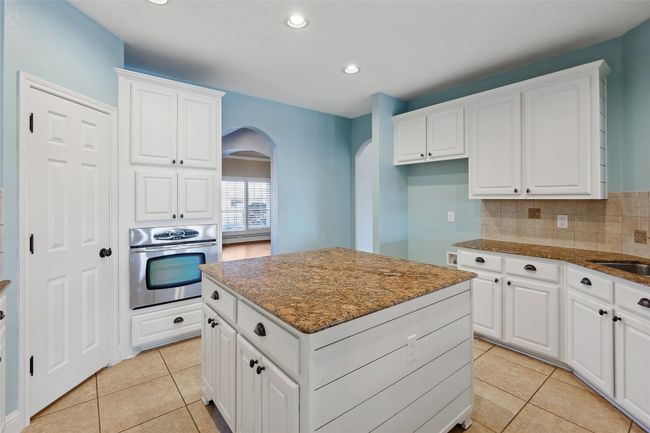 Kitchen with white cabinetry, oven, dark stone counters, and a kitchen island | Image 15