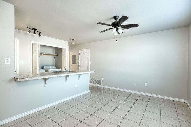 Kitchen featuring tile counters, a breakfast bar area, ceiling fan, light tile patterned floors, and electric panel | Image 4
