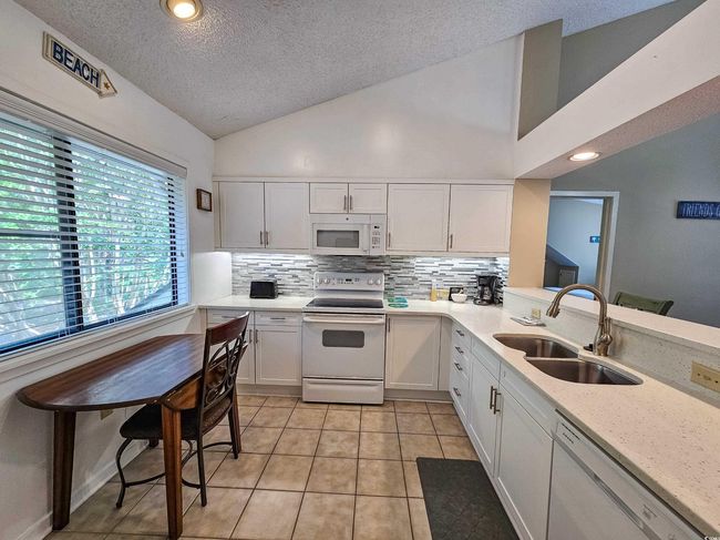 Kitchen featuring white appliances, a sink, a textured ceiling, backsplash, and white cabinets | Image 12