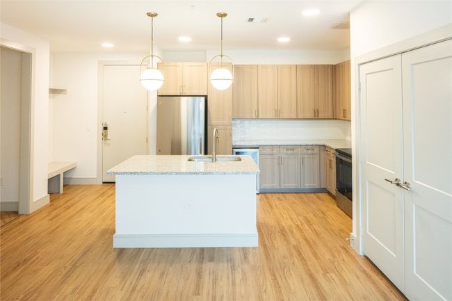 Kitchen with light wood finished floors, stainless steel appliances, visible vents, a sink, and an island with sink | Image 9