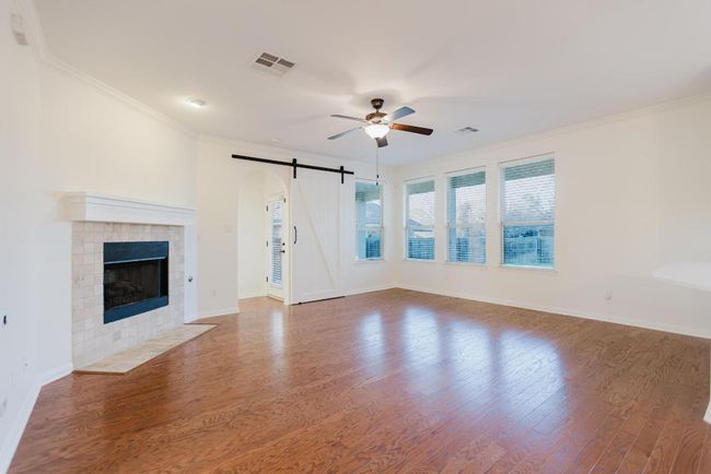 Unfurnished living room with wood finished floors, visible vents, ornamental molding, ceiling fan, and a barn door | Image 8