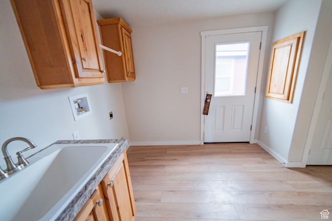 Laundry area with a sink, light wood-type flooring, hookup for a washing machine, electric dryer hookup, and cabinet space | Image 39