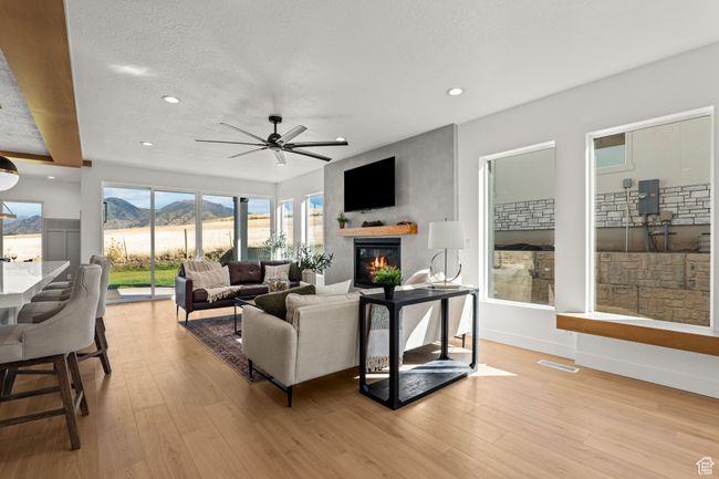 Living area featuring a textured ceiling, light wood-style floors, a glass covered fireplace, recessed lighting, and ceiling fan | Image 11