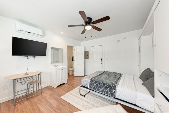 Bedroom with a wall mounted air conditioner, light wood finished floors, electric panel, connected bathroom, and ceiling fan | Image 7