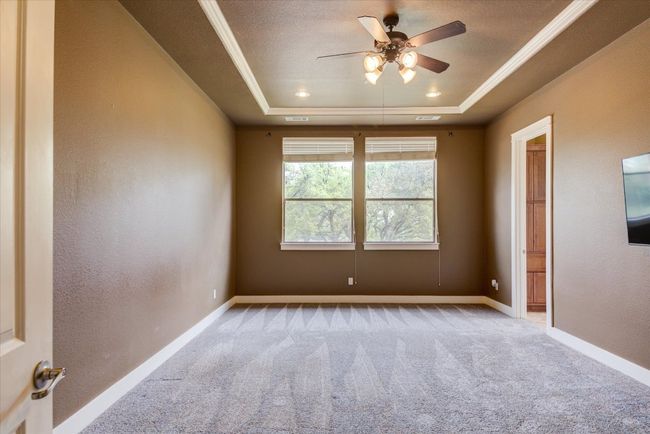 Primary bedroom with carpet flooring, ceiling fan, ornamental molding, and a tray ceiling | Image 16