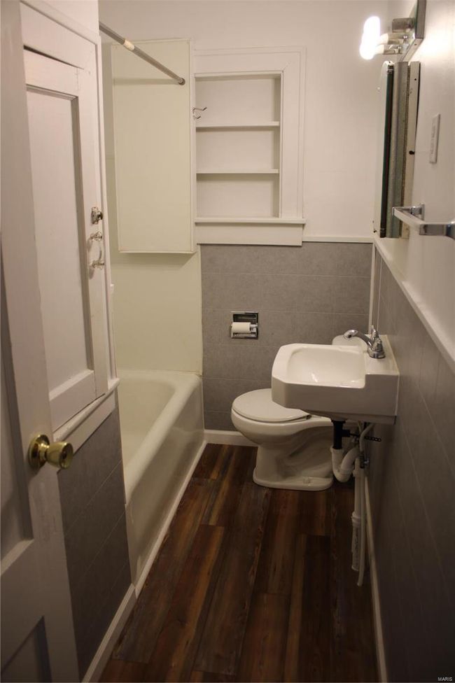 Full bathroom featuring toilet, a sink, wood finished floors, tile walls, and wainscoting | Image 7