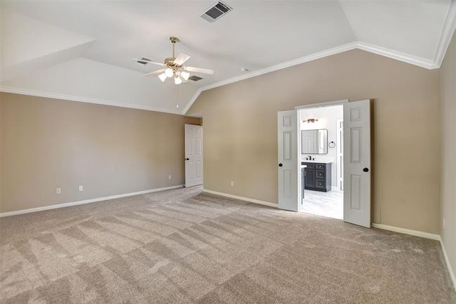 This spacious, carpeted bedroom features a ceiling fan, neutral walls, and crown molding. Double doors lead to an en-suite bathroom, adding convenience and style. | Image 33