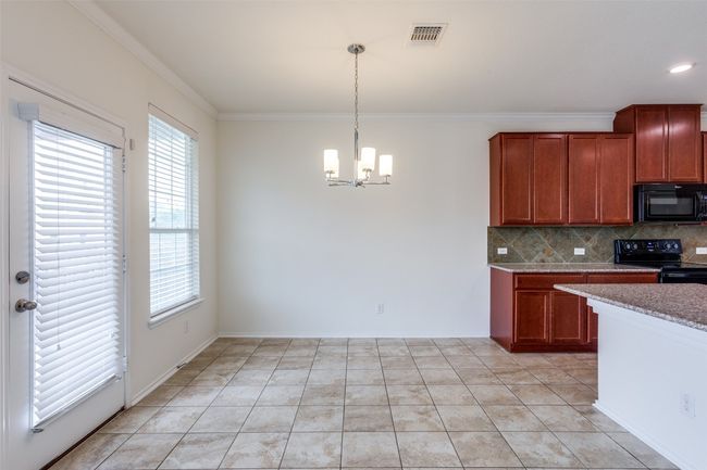 Kitchen featuring crown molding, an inviting chandelier, tasteful backsplash, visible vents, and black appliances | Image 11