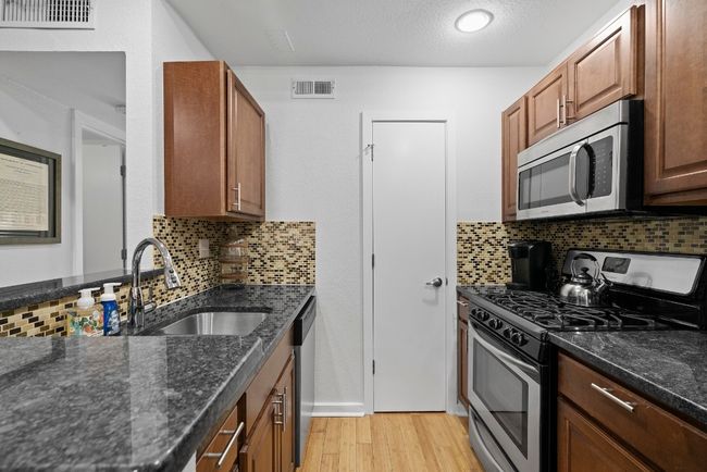 Kitchen with stainless steel appliances, a sink, light wood-style flooring, and decorative backsplash | Image 13
