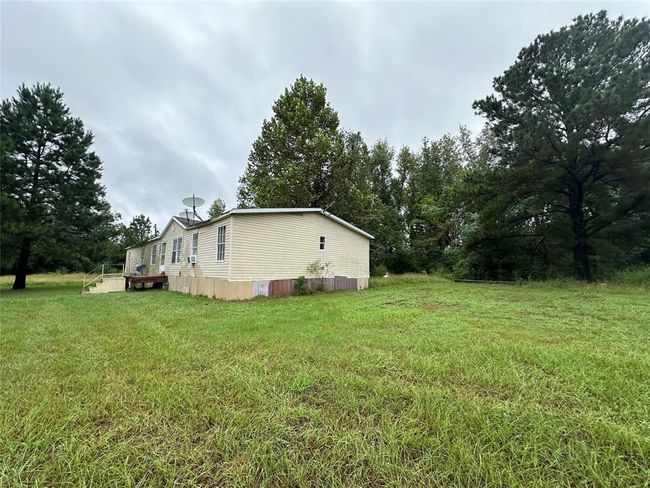 This photo shows a single-story home with light-colored siding, surrounded by a spacious, grassy yard and mature trees, offering a secluded and natural setting. | Image 11